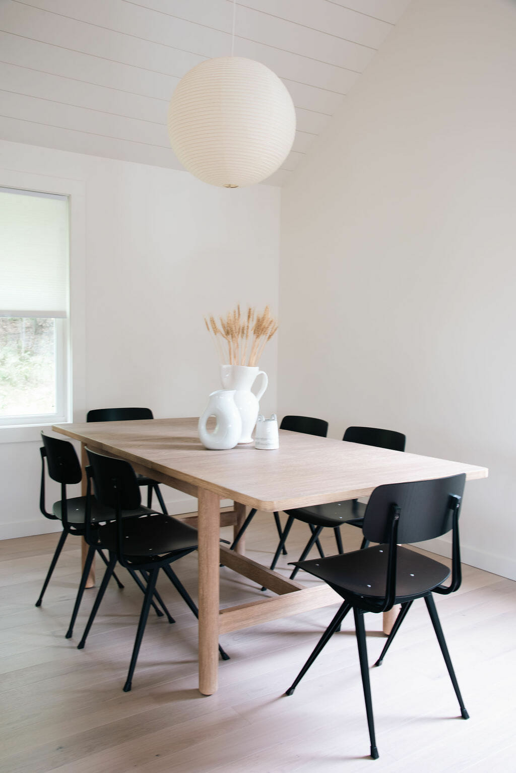 Light wood table with six black chairs around it and a globe shaped ceiling light overhead
