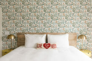 King sized bed white linens natural wood bed with two brass modern lamps on either side with love pillow red and white on bed