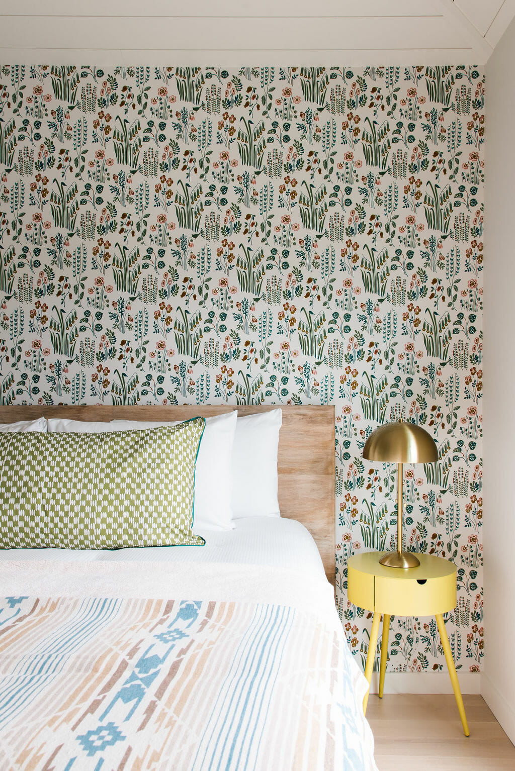 detail of king sized bed with one bed side table and brass lamp patterned wallpaper